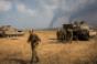 Israeli soldiers stand near their tank while smoke due to airstrikes and shelling rises from the Gaza Strip